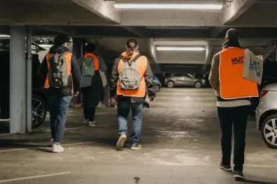 Photo de quatre bénévoles de la Nuit de la solidarité vus de dos, marchant dans un parking