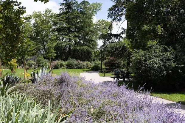 des personnes assises sur un banc, les massifs fleuris et les arbres du jardin des Barrières