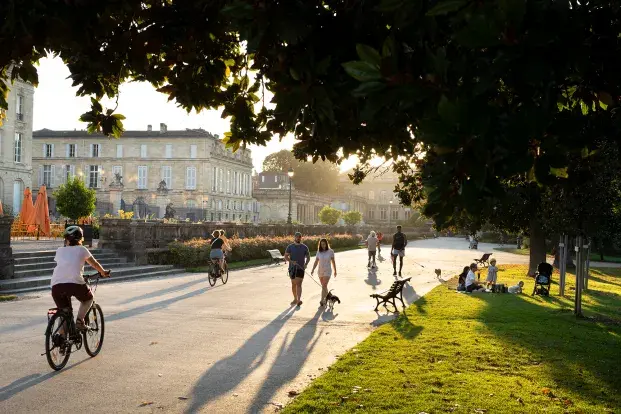 Un parc urbain animé sous une lumière dorée, avec promeneurs, cyclistes et pique-niqueurs.