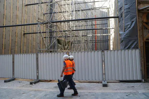 Des ouvriers portant des gilets oranges devant des échafaudages.