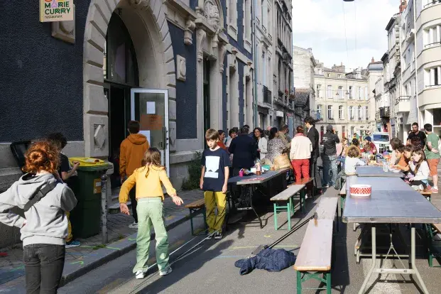 Des familles avec enfant, des tables et des banc lors d'un repas de quartier dans la rue