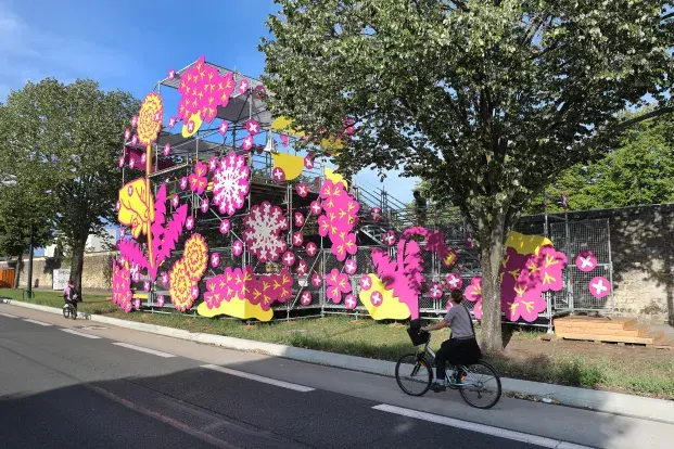 Photo de l'installation "Au delà des boulevards": une structure avec des dessins roses et jaunes, et une cycliste, sur les boulevards