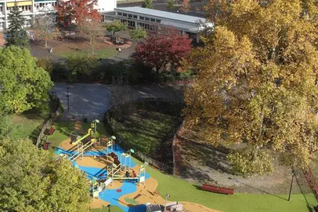 C’est une vue d’en haut d’un parc avec des jeux colorés pour enfants, des arbres et des bâtiments en arrière-plan.