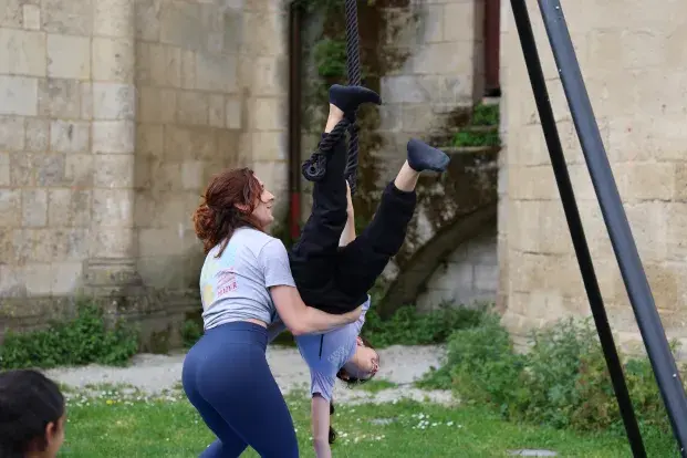 Photo d'une médiatrice chargé de l'atelier "Trapèze" aide une jeune fille à tenir en équilibre sur le trapèze