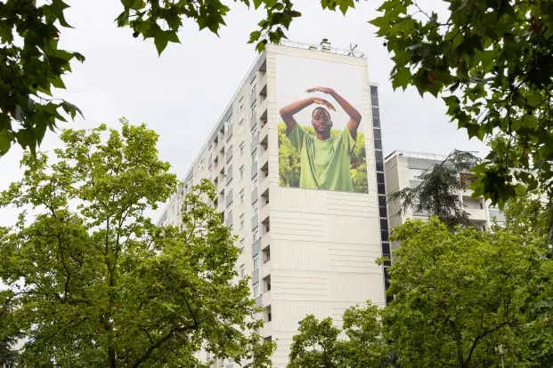 Photo d'une exposition grand format, avec une photographie sur le côté d'un immeuble. Un homme lève les bras sur la photo.