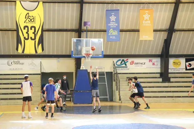 Photo de basketteurs tentant de mettre un panier, dans un gymnase.