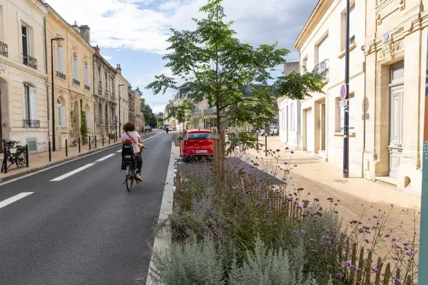 Photo d'une rue avec des trottoirs réaménagés, de la végétalisation et une cycliste de dos.