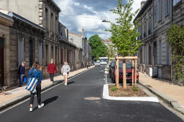 photo de la rue jean mermoz réaménagée avec des arbres plantés sur la droite. Des passants sur la gauche.
