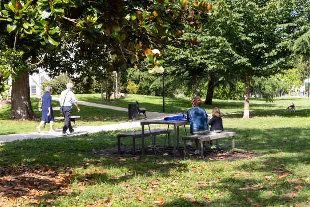 photo d'un square, avec des personnes assises autour d'une table de pique-nique, et des passants.