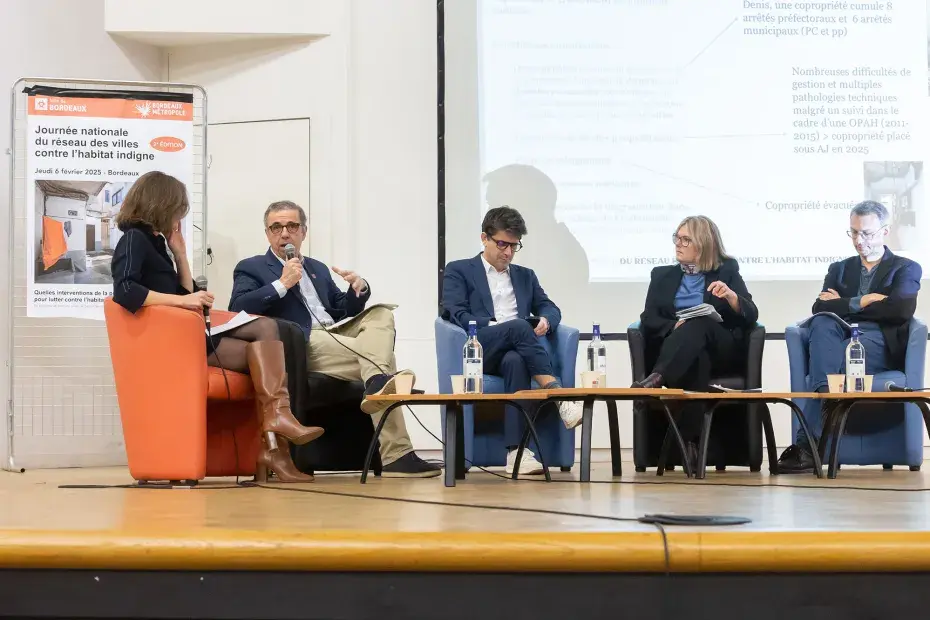 Le maire de Bordeaux, Pierre Hurmic, aux côtés de son homologue de Saint-Denis, Mathieu Hanotin, assis dans des fauteuils sur la scène de l'Athénée municipal.