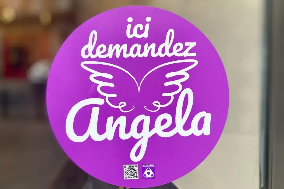 Photo d'un autocollant "Ici, demandez Angela" sur une vitrine de magasin de Bordeaux