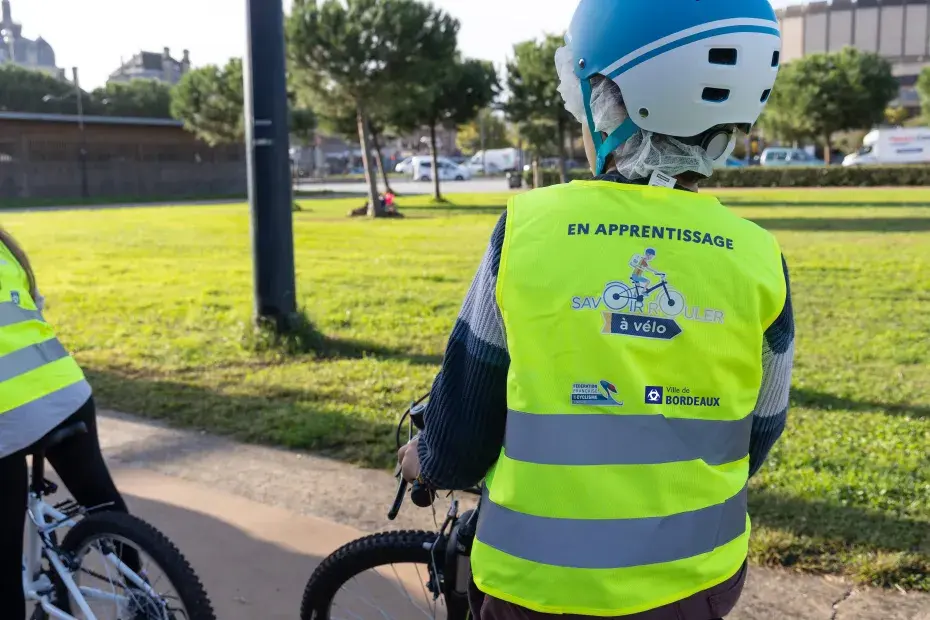 Photo d'un enfant à vélo portant un gilet jaune et un casque dans un parc.
