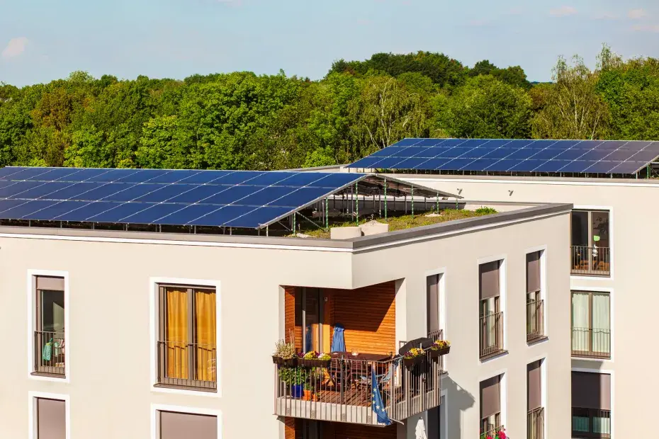 Photo d'un immeuble récent avec des panneaux solaires sur le toit et de la végétalisation en arrière plan.