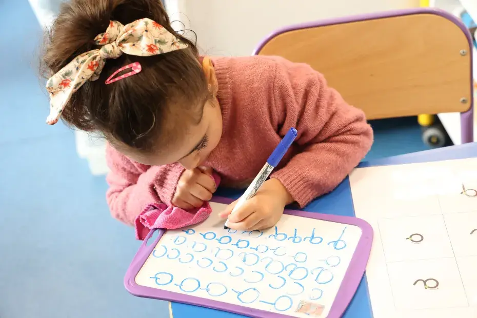une enfant fait des exercices d'écriture au feutre sur une ardoise blanche