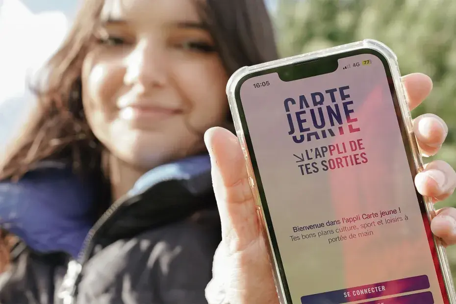 La photo montre un téléphone tenu par une jeune fille qui affiche la plateforme de la carte jeune en ligne