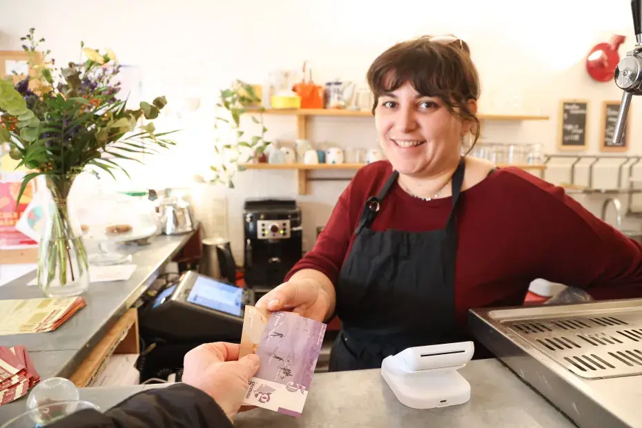 Une commerçante souriante reçoit un paiement en monnaie locale dans un café.