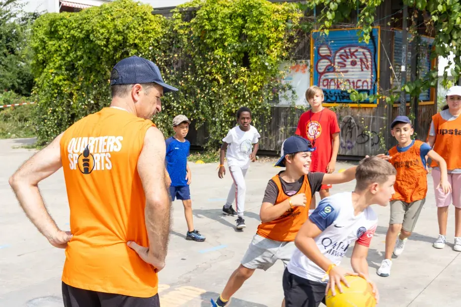 Un groupe d'enfant jour au basket sous la surveillance d'un animateur.