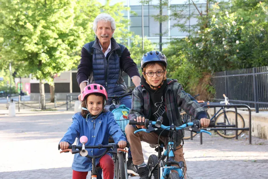 Un homme âgé accompagne ses petits enfants à vélo.