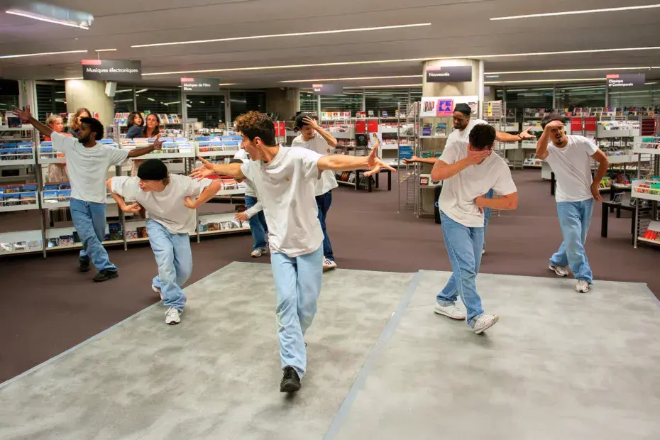 Groupe de jeunes danseurs tous habillés de la même façon, faisant une chorégraphie dans une bibliothèque