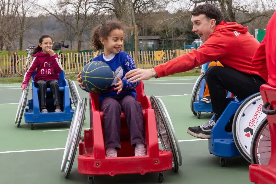 Deux jeune filles et un accompagnateur jouent au basket fauteuil.