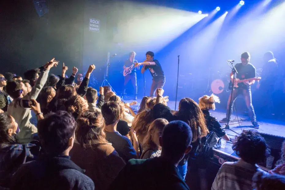 photo d'un concert de rock avec un public et des musiciens sur une scène.