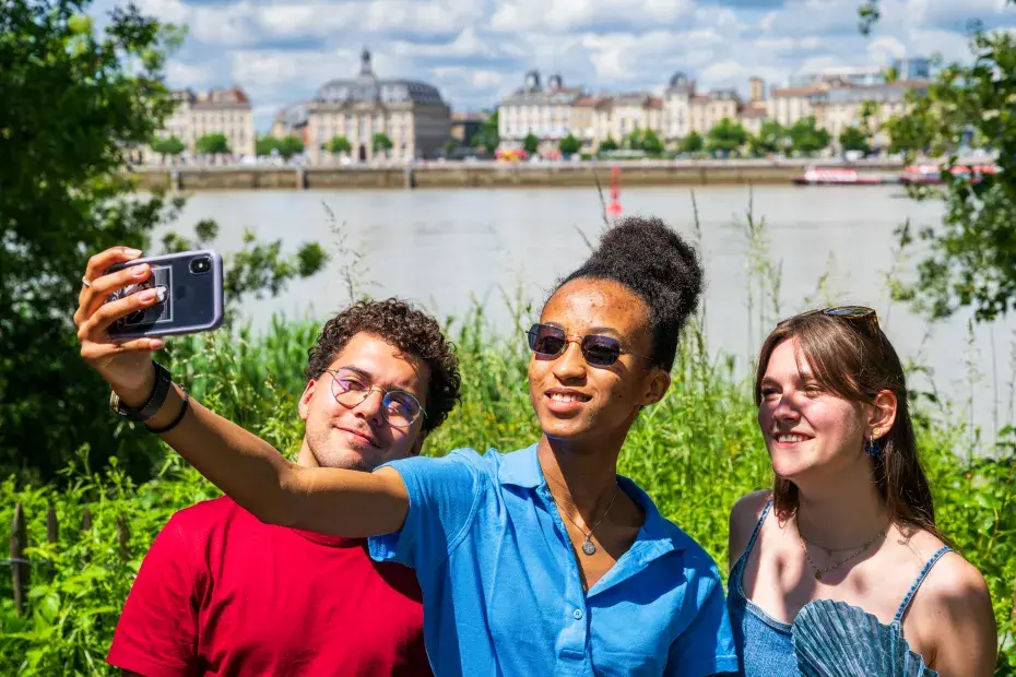 3 jeunes font un selfie devant la garonne et les quais de bordeaux depuis le parc aux angéliques