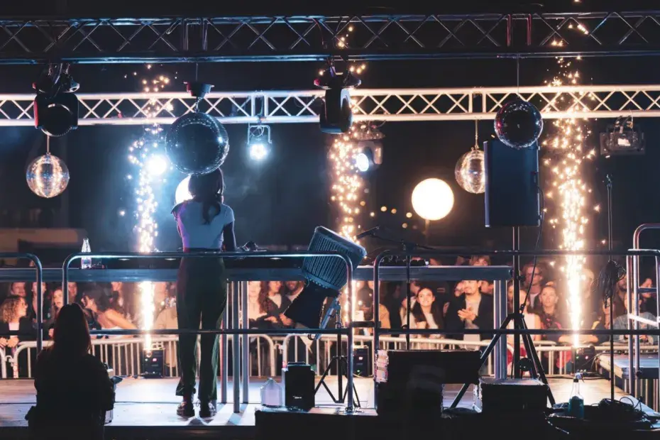 On aperçoit un DJ sur une scène durant un festival devant des spectateurs qui font la fête.