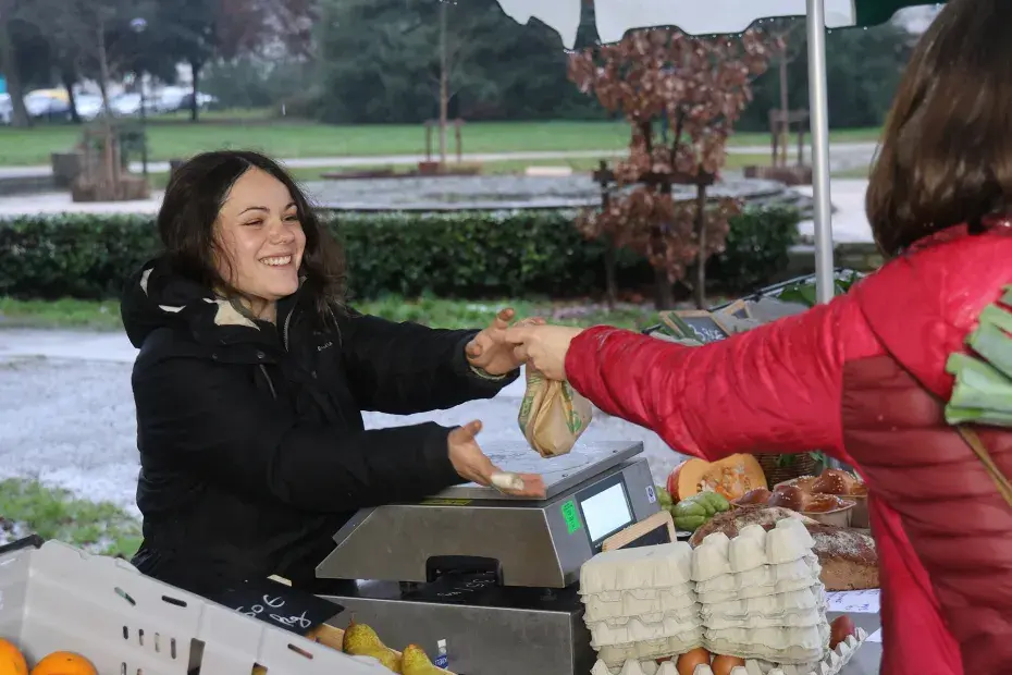 Une jeune vendeuse des "Jardins Garonnais" tend avec un grand sourire un sachet contenant des fruits qu'elle a récupéré sur son stand à sa cliente 