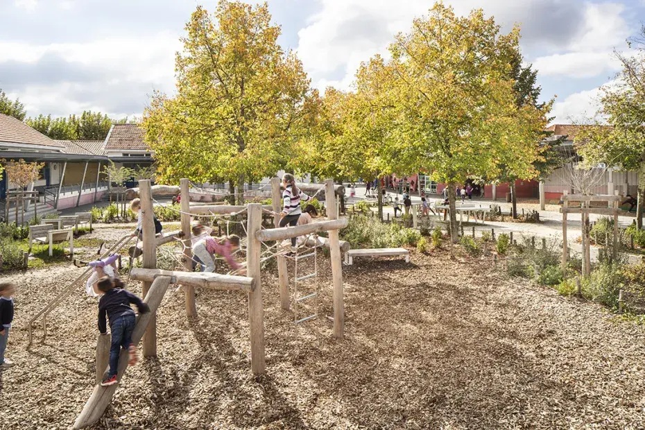 Des enfants jouent sur une structure en bois dans une cour d'école.
