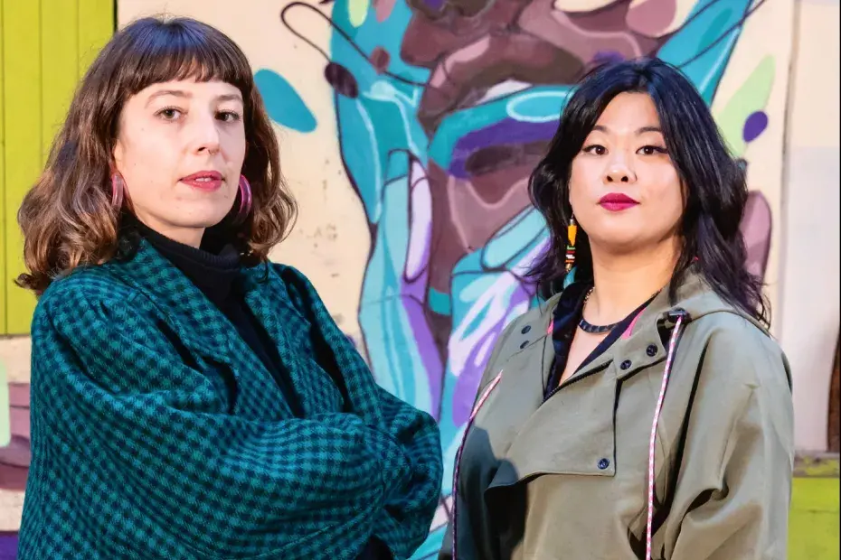 Photo de deux femmes devant un graff sur un mur