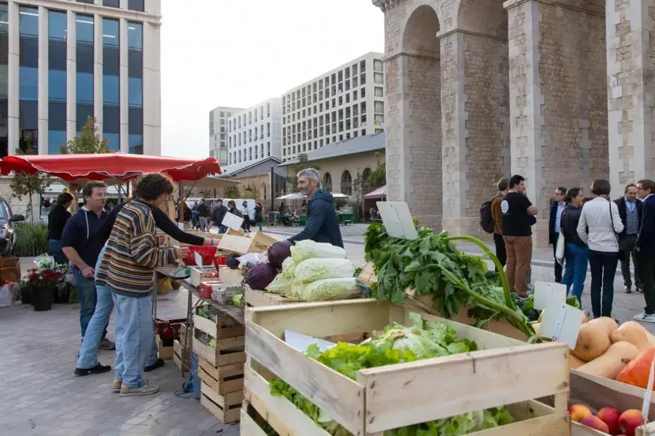 Un marché en plein air installé sur une place urbaine, devant un bâtiment en pierre