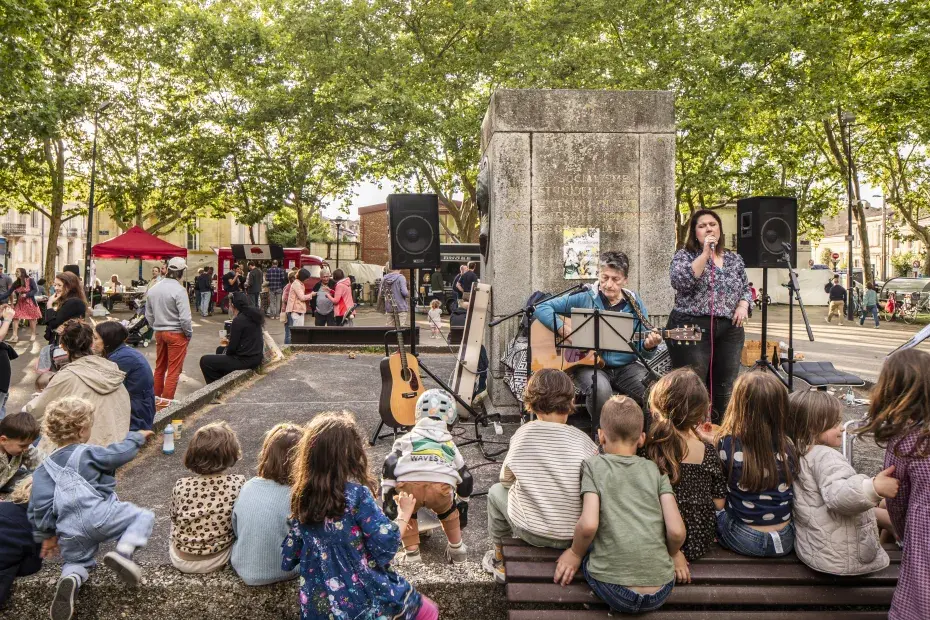 Photo d'un concert sur la place Calixte Camelle avec un guitariste et du public.
