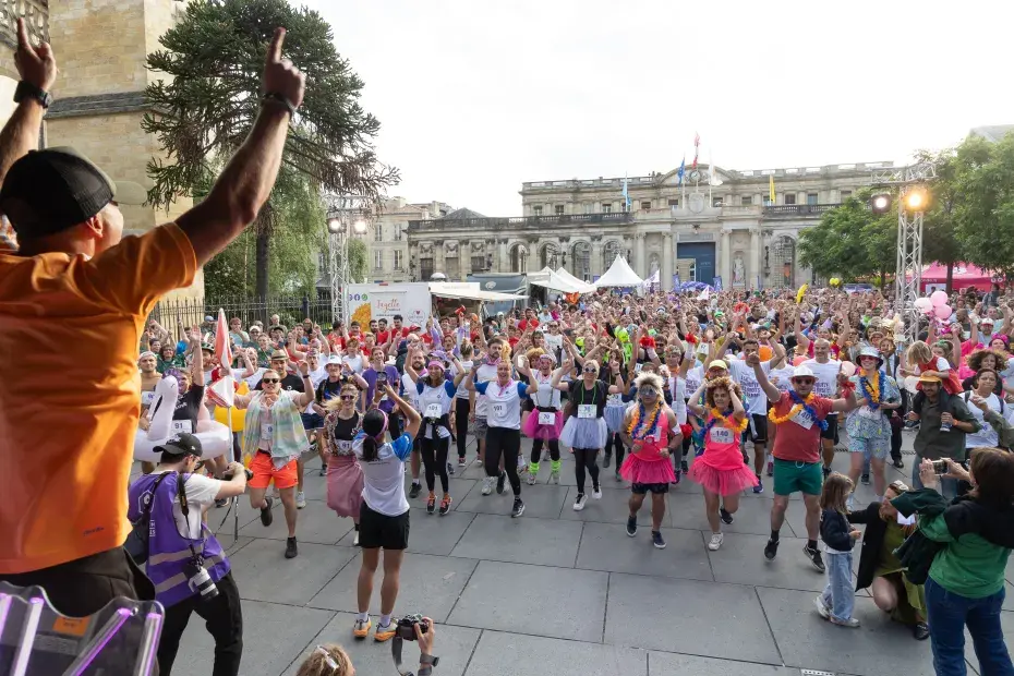 Photo des participants de la 4ème édition de la Nuits des relais. Les coureurs sont tous réunis devant un animateur les bras en l'air sur la place Pey-Berland