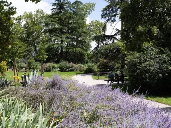 des personnes assises sur un banc, les massifs fleuris et les arbres du jardin des Barrières