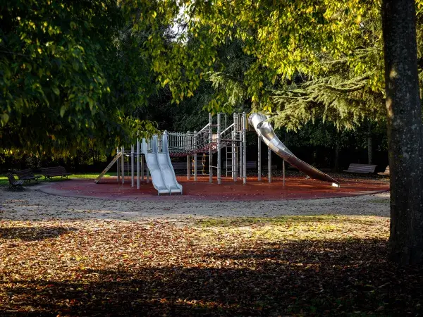 Une aire de jeux vide entourée d’arbres, baignée par une lumière automnale.