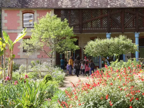 Un groupe d'enfants et d'adultes se rassemble devant une maison entourée d'un jardin, rempli de fleurs colorées et de plantes verdoyantes.