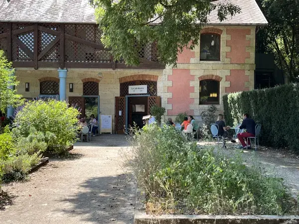 Un café en plein air devant une maison en pierre et en bois, avec des personnes assises à des tables entourées de verdure.