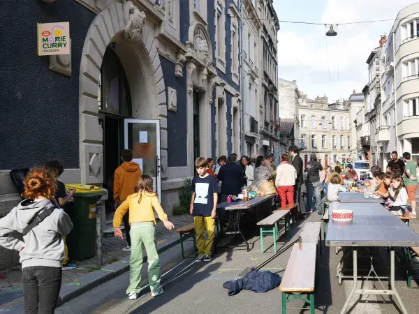 Des familles avec enfant, des tables et des banc lors d'un repas de quartier dans la rue