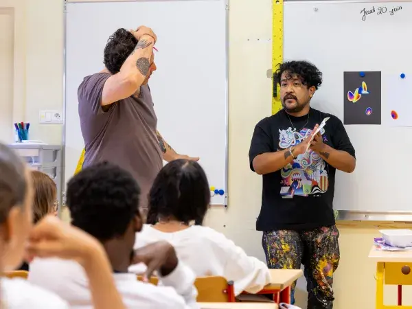 Photo de l'artiste Xomatok face devant des élèves assis à leur bureau dans leur classe.