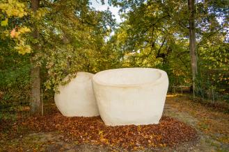 Deux grandes sculptures blanches en forme de bols reposent sur un lit de feuilles d'automne dans une forêt.