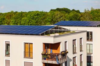 Photo d'un immeuble récent avec des panneaux solaires sur le toit et de la végétalisation en arrière plan.