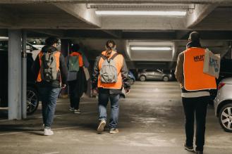 Photo de quatre bénévoles de la Nuit de la solidarité vus de dos, marchant dans un parking