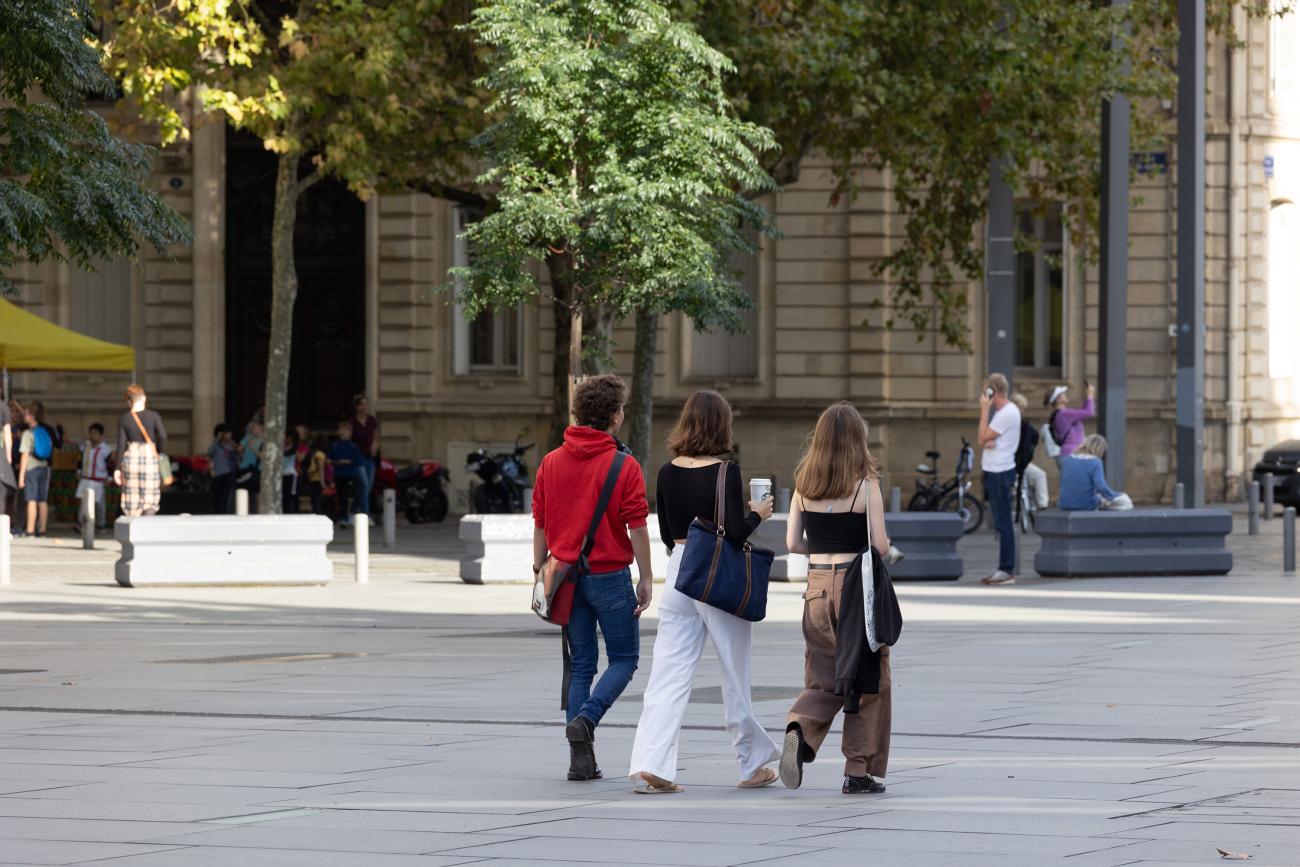 Un groupe de trois personnes composé d'un homme et deux femmes marchent sur la place Pey-Berland à Bordeaux.