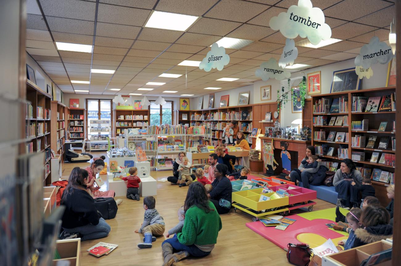 Une bibliothèque animée où enfants et adultes participent à une lecture collective au milieu des livres.